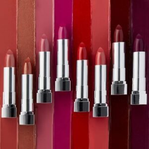 Row of colorful lipsticks with silver cases in varying reds, pinks, and purples against matching lipstick tubes