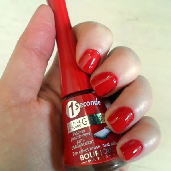 bourjois vernis a ongles 1 seconde gel 1 – BEAUTÉNIUM BeautÉnium Hand Holding a Red Bourjois Paris Nail Polish Bottle Labeled 1 Seconde with Bright Red Nails Painted on Fingers Visible in the Foreground